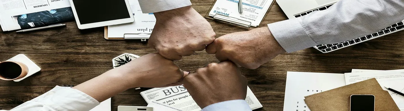 Team members bumping fists over a desk with laptops and documents